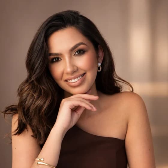 Dra. Márcia Morais sorrindo, com roupa marrom e a mão apoiada sob o queixo